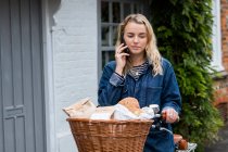 Mujer rubia joven en bicicleta con cesta, hablando por teléfono móvil. - foto de stock