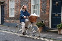 Joven mujer rubia en bicicleta por una calle del pueblo. - foto de stock