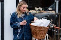 Jeune femme blonde debout à côté de vélo à l'extérieur des déchets magasin d'aliments complets gratuit. — Photo de stock