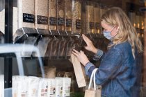 Young blond woman wearing face mask, shopping in waste free wholefood store. — Stock Photo