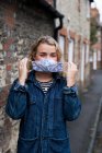 Young blond woman standing outdoors, putting on face mask. — Stock Photo