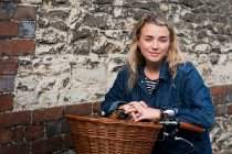 Young blond woman on bicycle with basket, looking at camera. — Stock Photo