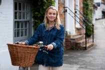 Young blond woman on bicycle with basket, looking at camera. — Stock Photo