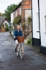 Jovem mulher loira pedalando por uma rua da aldeia. — Fotografia de Stock