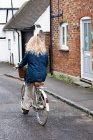 Rear view of young blond woman cycling down a village street. — Stock Photo