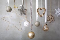 Christmas decorations, silver, white and gold baubles on ribbons on grey background. — Stock Photo