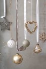 Christmas decorations, silver, white and gold baubles on ribbons on grey background. — Stock Photo
