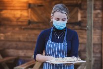 Woman waitress in apron and face mask holding plate of pizza. — Stock Photo