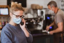 Блондинка в маске, работает в кафе, разговаривает по телефону. — стоковое фото