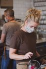 Blonde Kellnerin mit Gesichtsmaske arbeitet in einem Café. — Stockfoto