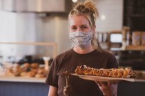 Blonde Kellnerin mit Mundschutz arbeitet in einem Café und trägt Teller mit Essen. — Stockfoto