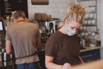 Блондинка офіціантка в масці для обличчя, що працює в кафе . — стокове фото
