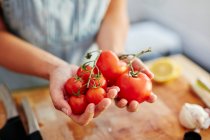 Woman holding different sized organic tomatoes in kitchen — Stock Photo