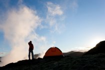 Женщина, стоящая у палатки на рассвете, Исландия — стоковое фото