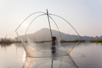 Pescador en su barco moviendo redes batientes arqueadas sobre el agua en el lago Loktak - foto de stock