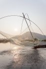 Pescador en su barco moviendo redes batientes arqueadas sobre el agua en el lago Loktak - foto de stock
