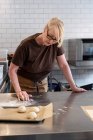 Mujer en delantal marrón de pie en una cocina cafetería, mezclando masa de pastelería danesa para hornear - foto de stock