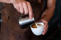 Close up de barista vestindo avental marrom derramando cappuccino. — Fotografia de Stock