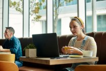Женщина, сидящая в кафе с ноутбуком, взаимодействующая во время онлайн-звонка — стоковое фото