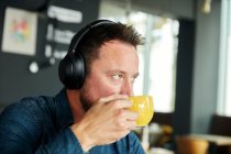 Hombre sentado en un café con auriculares, bebiendo café - foto de stock