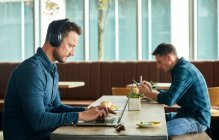 Два чоловіки сидять у кафе, працюють дистанційно за допомогою ноутбука та смартфона — стокове фото