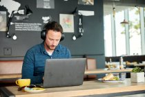 Homem sentado em um café, trabalhando em um laptop — Fotografia de Stock