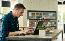 Homem sentado em um café, trabalhando em um laptop — Fotografia de Stock