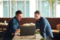 Двое мужчин сидят в кафе и смотрят на экран ноутбука. — стоковое фото