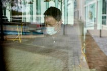 Man in a face mask sitting at a cafe table, view through a window — Stock Photo
