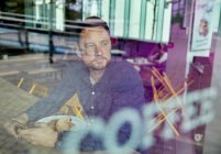 Человек в маске сидит за столиком кафе, смотрит в окно — стоковое фото