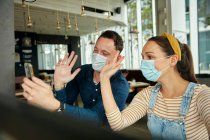 Two people wearing face masks, using a smart phone, waving during a face time call. — Stock Photo