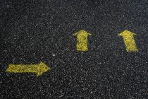 Alto ángulo de cerca de los símbolos de flecha amarilla pintados en el suelo de asfalto. - foto de stock