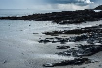 View of a sandy beach and rocky shore under a cloudy sky. — Stock Photo