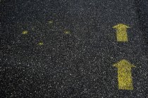 Ângulo alto perto de símbolos de seta amarelos pintados no chão de asfalto. — Fotografia de Stock