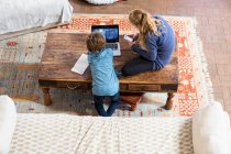 Overhead view of teenage girl and her younger brother using laptop and smart phone — Stock Photo