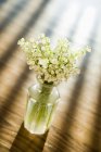 Lily of the valley flowers in glass vase on wooden table. — Stock Photo