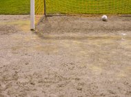 Balón de fútbol en la red de gol en el campo de fútbol fangoso. - foto de stock
