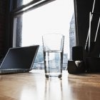 Laptop and drinking water glass on desk in urban office — Stock Photo