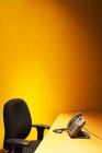 Стол со стулом, телефоном и желтой стеной позади — стоковое фото