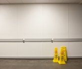 Предупреждающие конусы влажного пола с белой стеной позади — стоковое фото