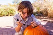 Young boy carving pumpkin on patio. — Stock Photo