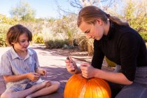 Teenage girl and her younger brother carving pumpkins on patio. — Stock Photo