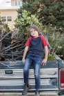 Young boy sitting on old pick up truck full of brushwood — Stock Photo