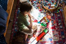 Garçon assis parmi les jouets sur le sol de sa chambre dans un patch de lumière du soleil — Photo de stock