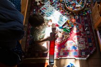 Ragazzo seduto tra i giocattoli sul pavimento della sua camera da letto in una macchia di luce solare — Foto stock