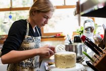 Дівчина-підліток на кухні, застосовуючи глазур до торта — стокове фото