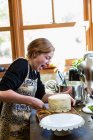 Девочка-подросток на кухне наносит глазурь на торт — стоковое фото