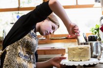 Adolescente en cocina aplicación de hielo a la torta - foto de stock
