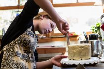 Teenage girl in kitchen applying icing to cake — Stock Photo