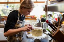 Девочка-подросток на кухне наносит глазурь на торт — стоковое фото